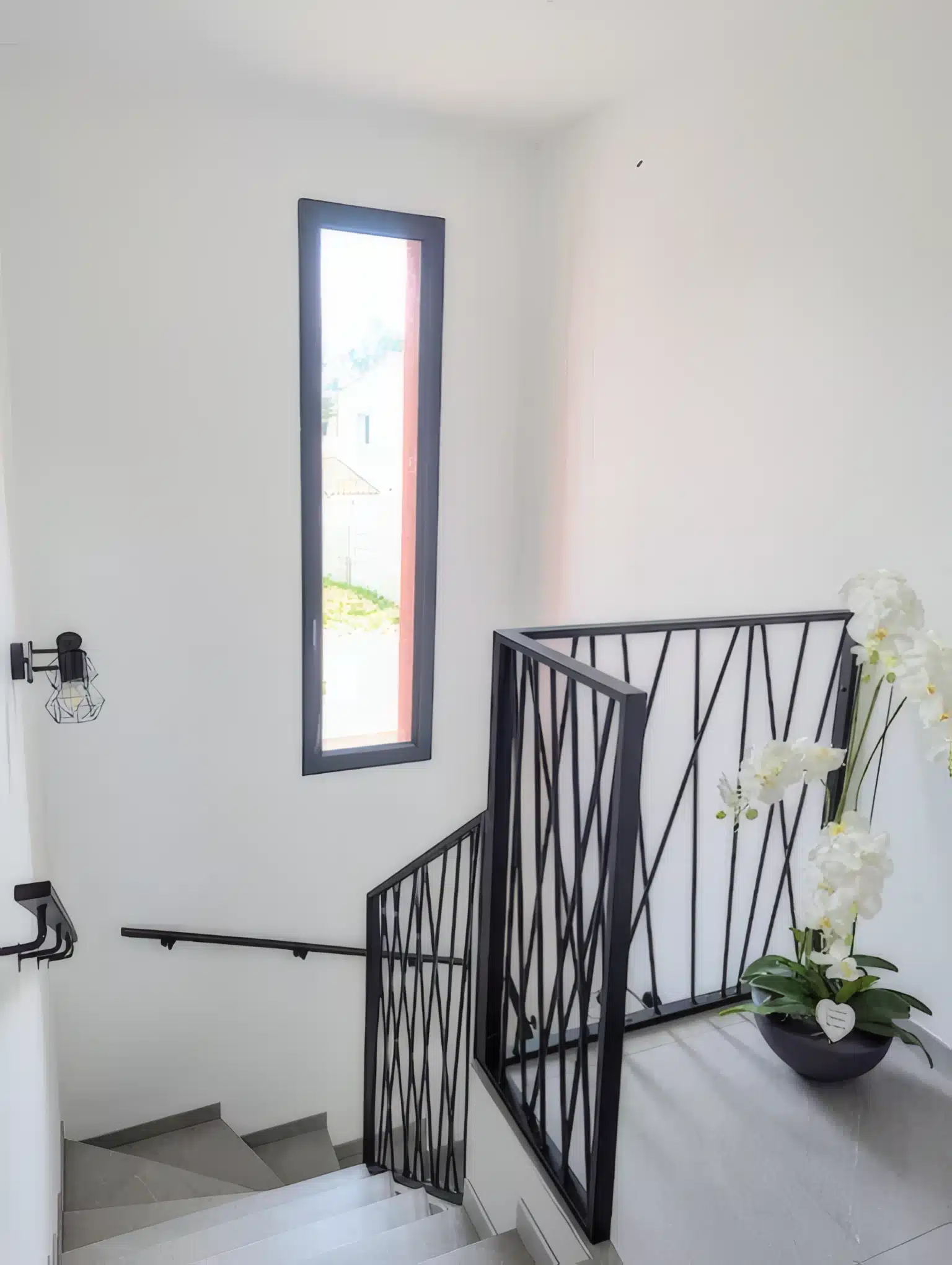 Garde-corps terrasse en fer forgé noir et mur en pierre Terrasse avec garde-corps en fer noir, carrelage effet bois et mur en pierre naturelle sur fond de forêt.